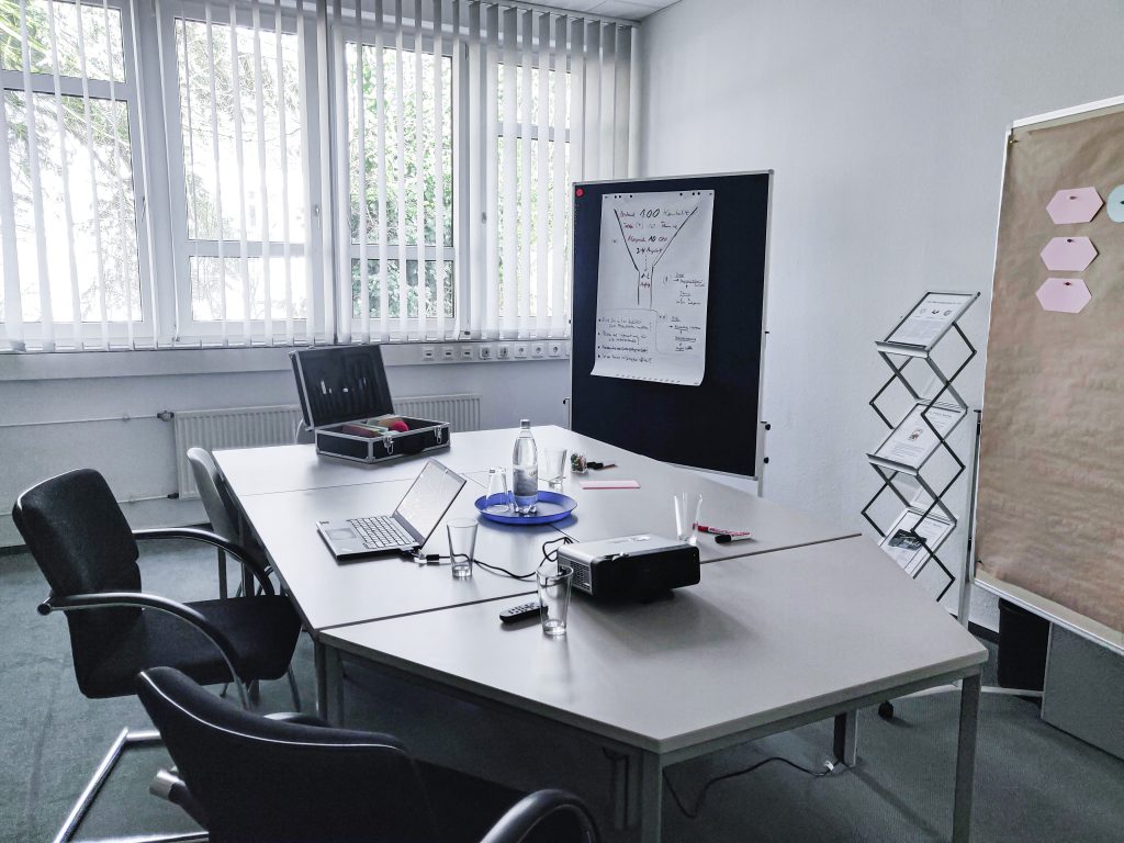 Ein Raum für Besprechungen und Meetings ausgestattet mit einem Beamer, Flipchart, Whiteboard, Moderationskoffer, einem Tisch und Stühle.